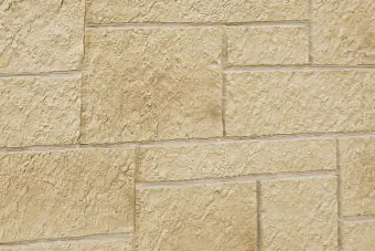 Close-up of a beige textured stone masonry wall with rectangular blocks and visible joints.