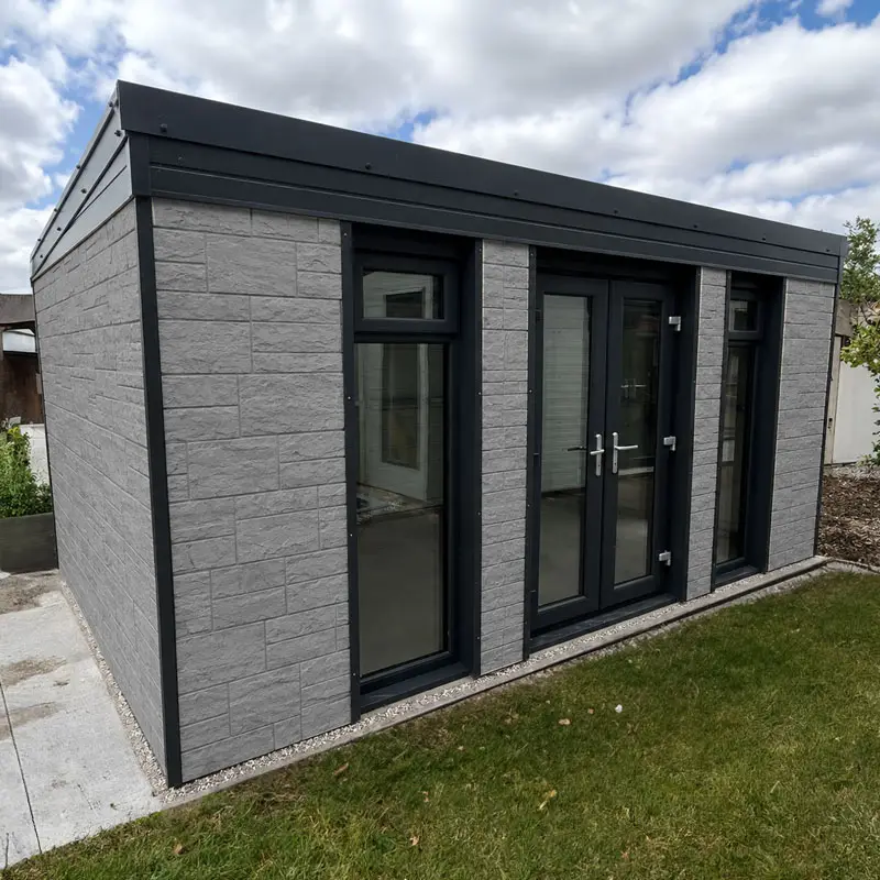 Modern grey brick outbuilding with three tall glass doors and windows, black frames, and a flat roof by a green lawn.
