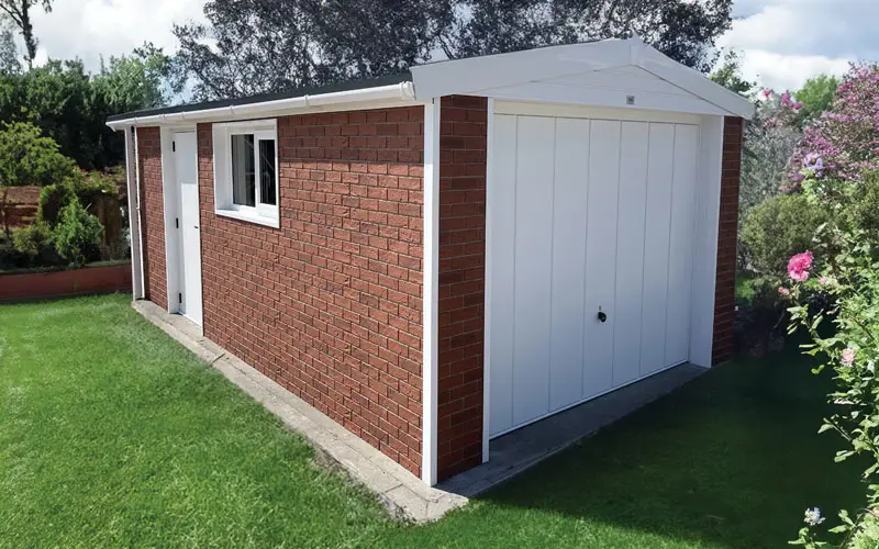 BRICK-CLAD-GARAGE - All Seasons Steel Buildings Brick garden shed with white double doors, white trim, and a side door against a grassy backyard with a window on the side wall.