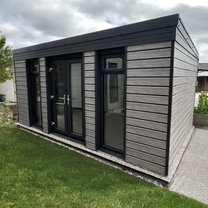 Modern garden shed with black-framed glass doors and grey horizontal wood siding in a lawn setting